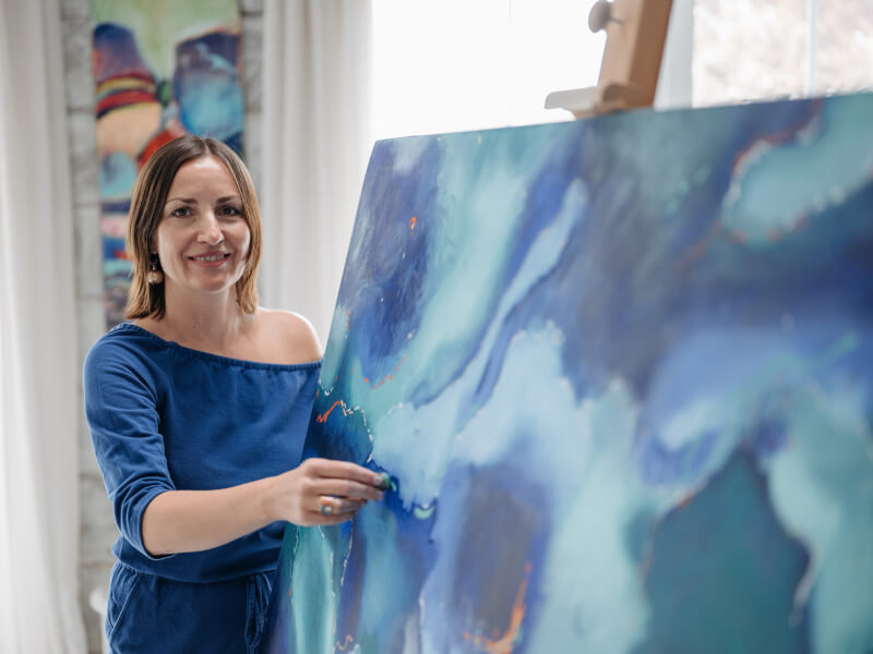 Woman smiling next to a canvas of fluid art